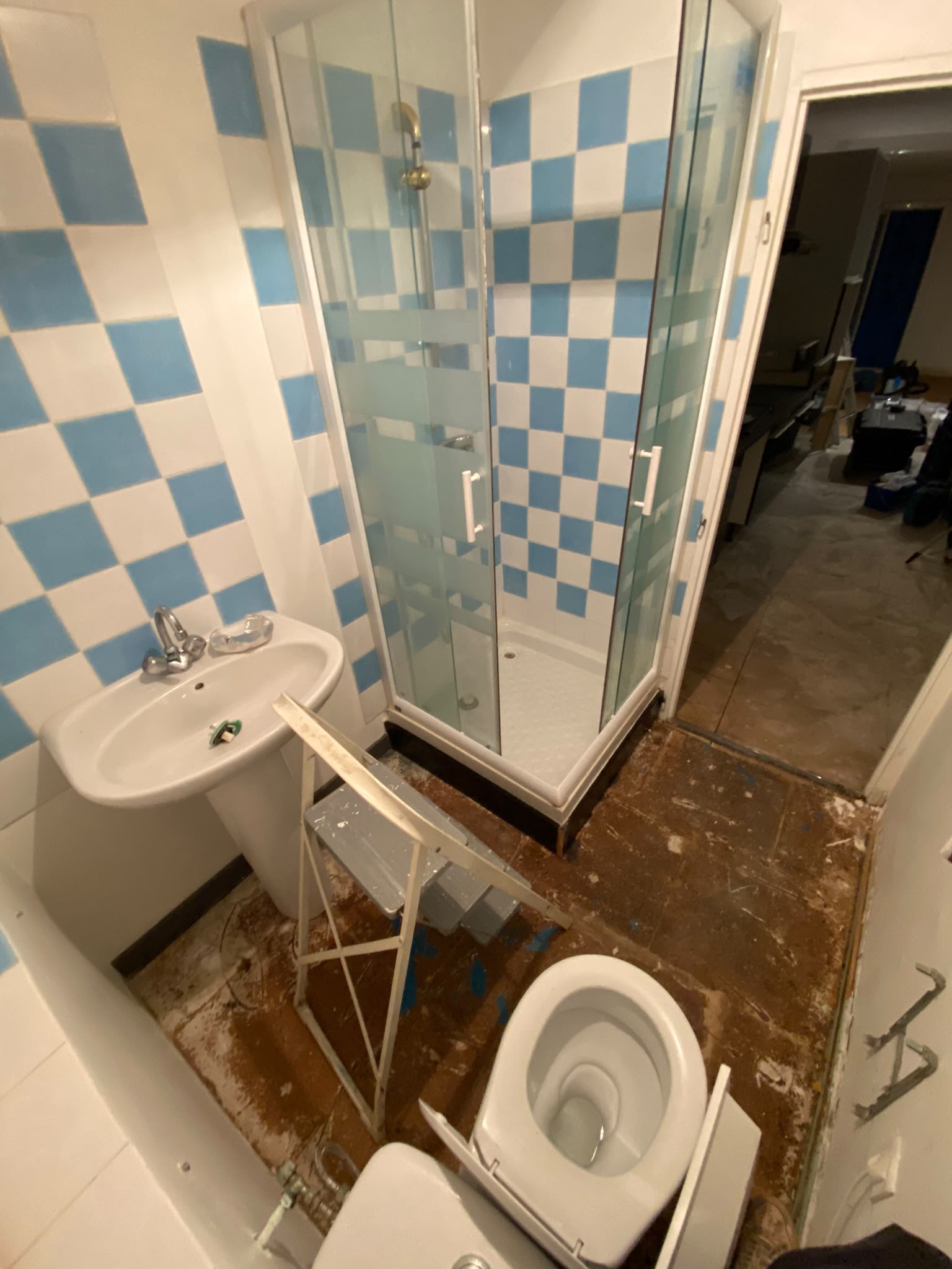 Salle de bain avant rénovation — carrelage damier bleu et blanc, cabine de douche vétuste