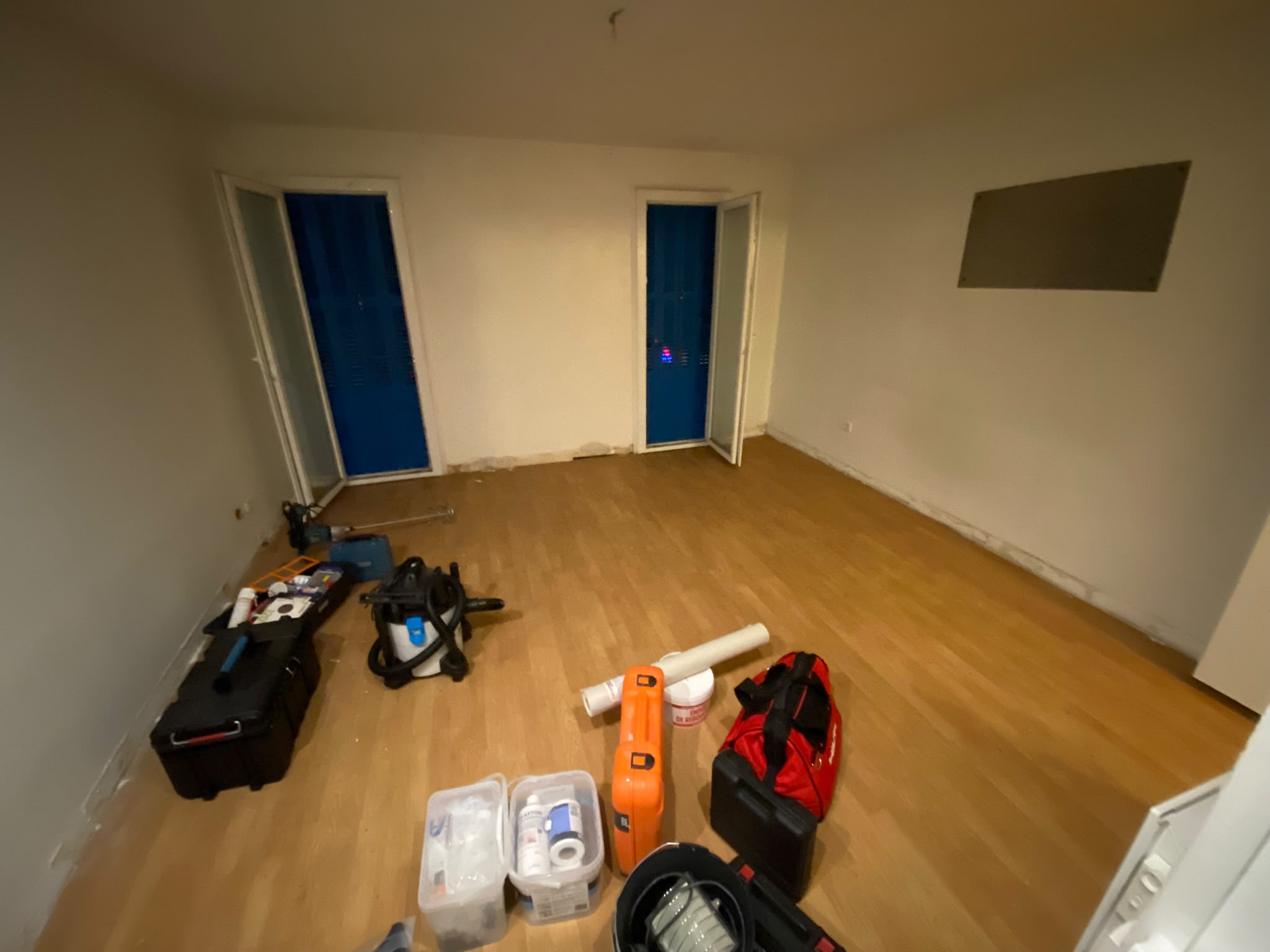 Pièce de vie avant rénovation — parquet usé, murs défraîchis, outillage de chantier