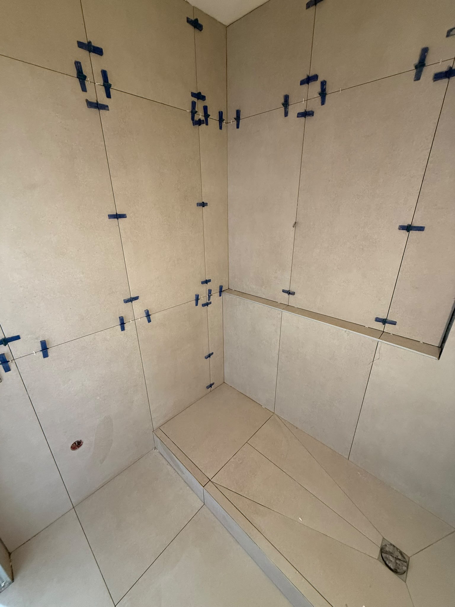 Pose de carrelage grand format dans une douche à l'italienne avec croisillons de nivellement
