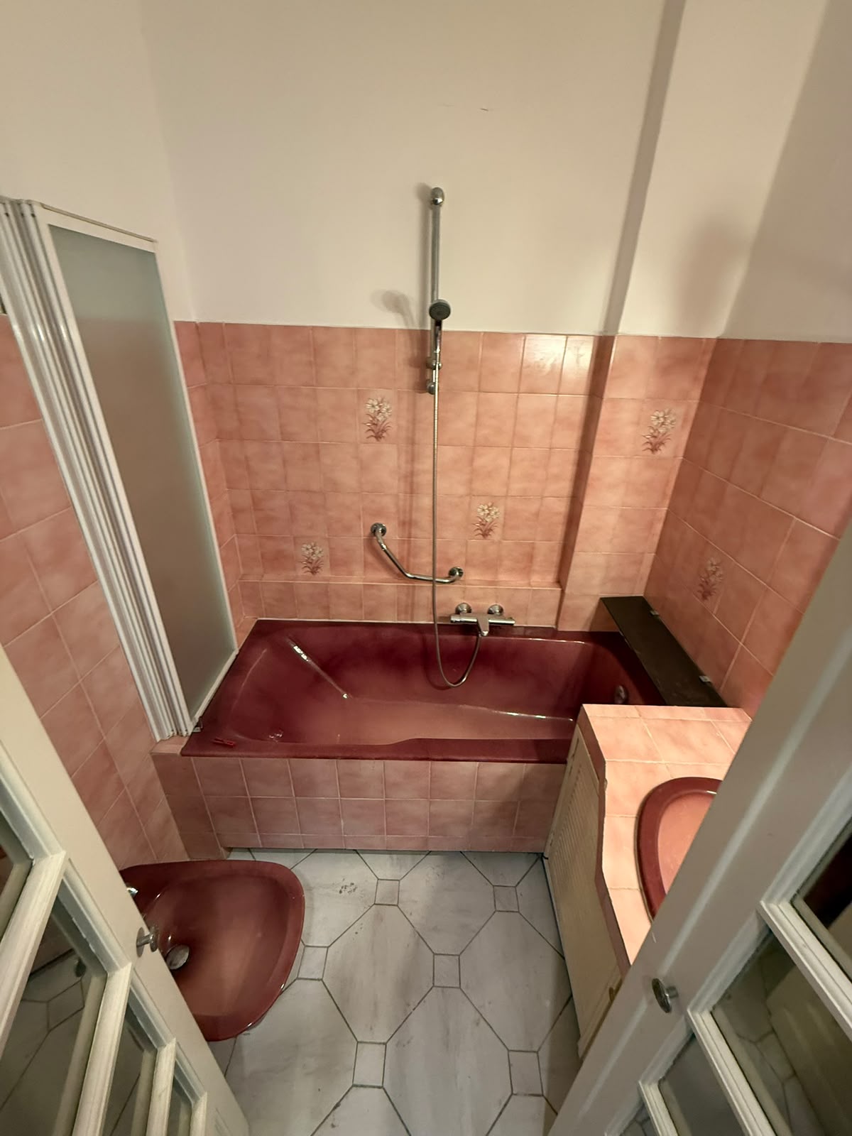 Salle de bain vétuste avec baignoire rose et carrelage daté