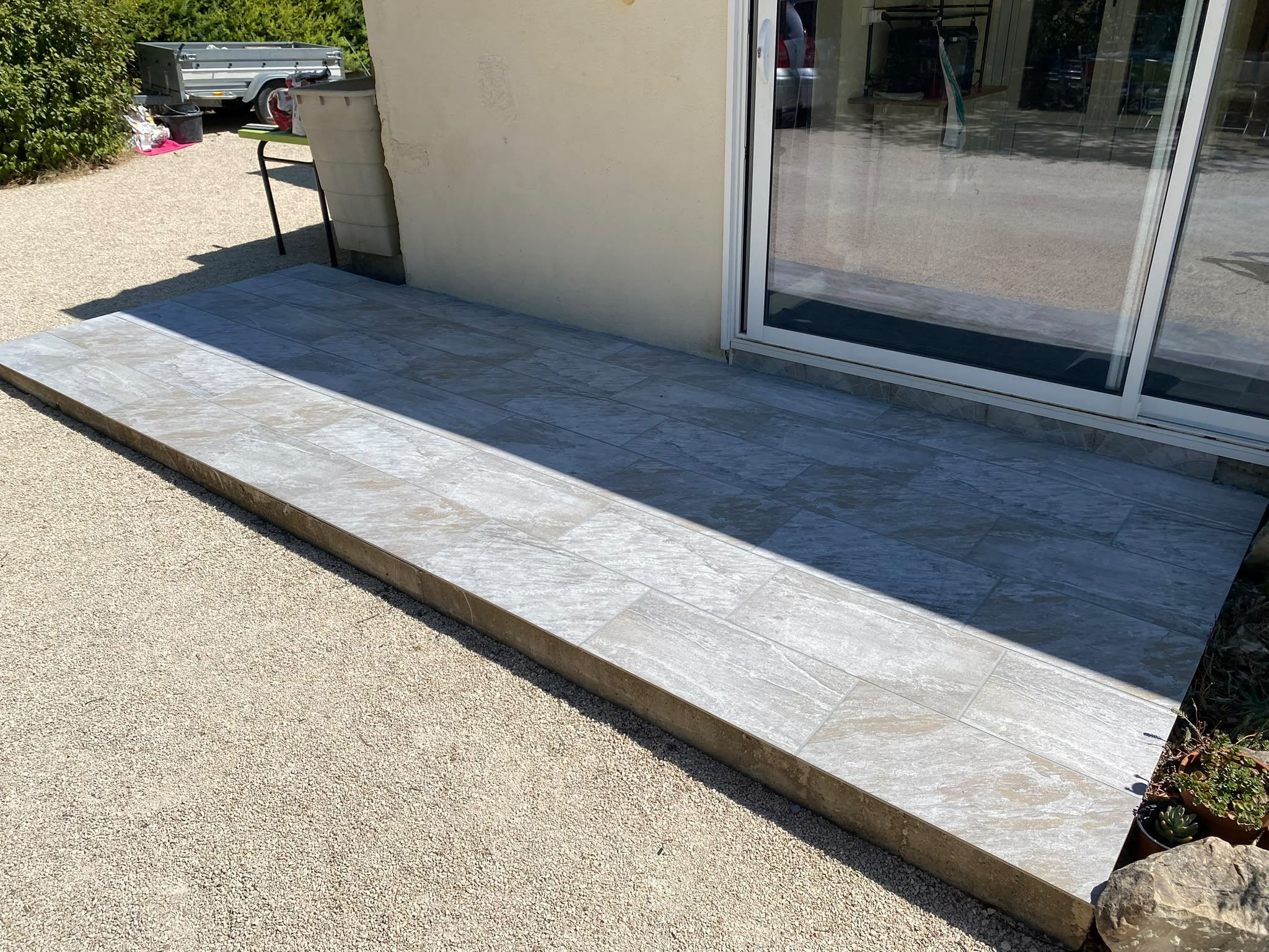 Détail de la dalle de terrasse avec carrelage effet pierre naturelle et baie vitrée